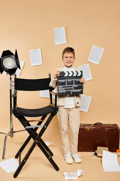 Preadolescent boy in film director attire holding clapper in front of chair. — Stock Photo
