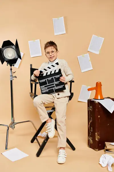 Menino pré-adolescente vestido como diretor, sentado e segurando uma ardósia de filme. — Fotografia de Stock
