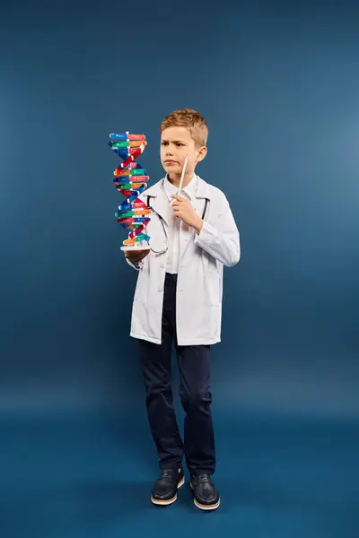 Preadolescent boy, dressed as a doctor, holds a model of a structure. — Stock Photo