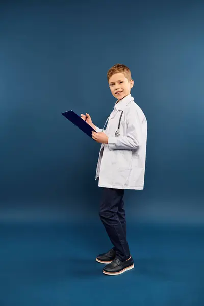 A preadolescent boy in a lab coat holding a clipboard. — Stock Photo