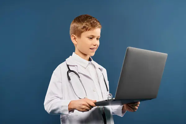 Un ragazzino, vestito da medico, si concentra sul suo portatile. — Foto stock