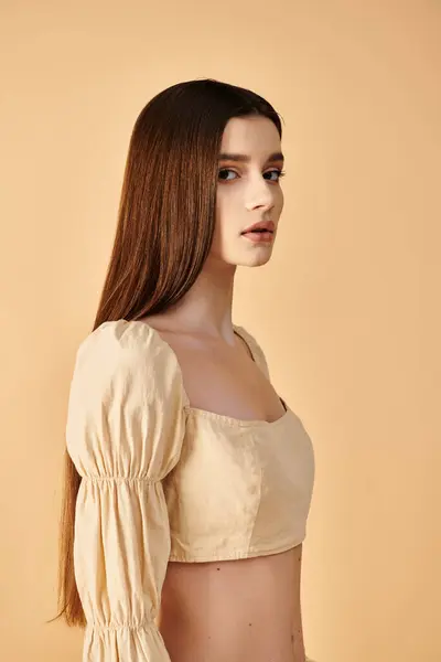 Une jeune femme aux longs cheveux bruns, incarnant une humeur estivale, pose gracieusement dans un haut blanc dans un décor de studio. — Photo de stock