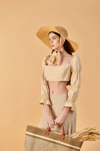 Une jeune femme aux longs cheveux bruns pose sereinement dans une tenue d'été, tenant un panier tout en portant un chapeau élégant. — Photo de stock