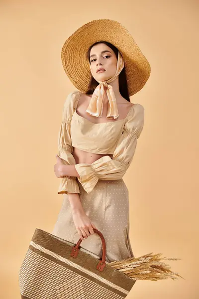 Stylish young woman with long brunette hair in a hat and dress holding a basket, embodying a summer vibe in a studio setting. — Stock Photo