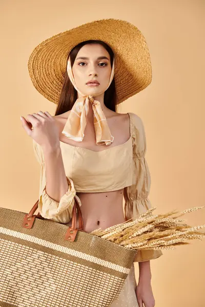 Una joven morena exuda elegancia veraniega, vistiendo un sombrero de paja y sosteniendo una elegante bolsa en un ambiente de estudio. - foto de stock