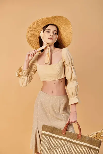 Mujer joven con el pelo largo y morena emana vibraciones de verano, sosteniendo una bolsa de paja en un elegante sombrero de paja. - foto de stock