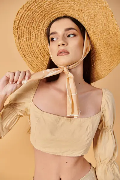 Une jeune femme avec de longs cheveux bruns frappant une pose dans un décor de studio, portant un chapeau de paille et un haut jaune vibrant exsudant des vibrations estivales. — Photo de stock