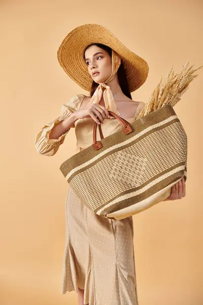 Mujer joven con el pelo largo morena golpeando una pose de verano, irradiando elegancia en un sombrero de paja mientras sostiene una bolsa. - foto de stock