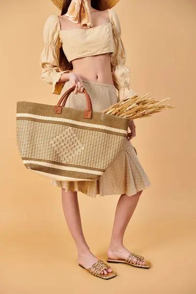 Une jeune femme aux longs cheveux bruns portant un chapeau de paille, tenant un sac, exsudant des vibrations estivales dans un décor de studio. — Photo de stock