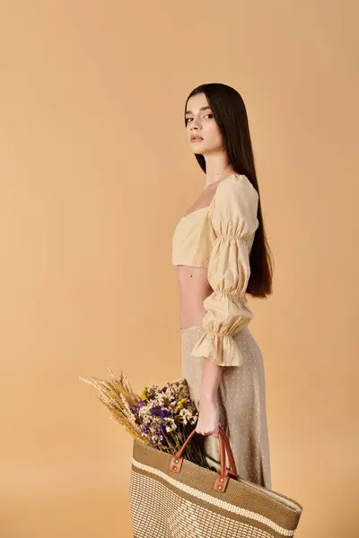 Una giovane donna con lunghi capelli castani posa in un vestito estivo, con un cesto pieno di fiori colorati. — Foto stock