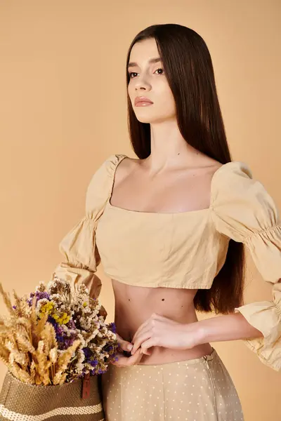 Eine junge Frau mit langen brünetten Haaren posiert in einem bauchfreien Oberteil und hält einen lebendigen Blumenstrauß in einem Studio-Setting. — Stockfoto