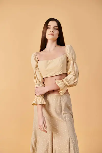 A young woman with long brunette hair poses gracefully in a summer outfit of a cropped top and skirt — Stock Photo