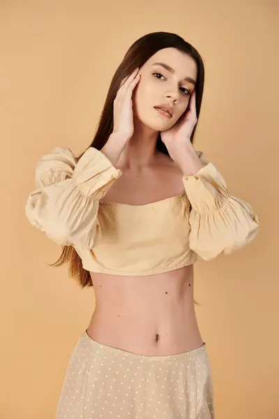 Eine junge brünette Frau posiert gelassen in einem Sommeroutfit, die Hände zart auf ihr Gesicht gelegt. — Stockfoto