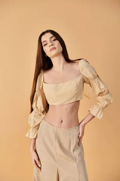 Une jeune femme aux longs cheveux bruns dégage des vibrations estivales dans un crop top élégant et un pantalon à larges pattes, frappant une pose dans un cadre de studio. — Photo de stock