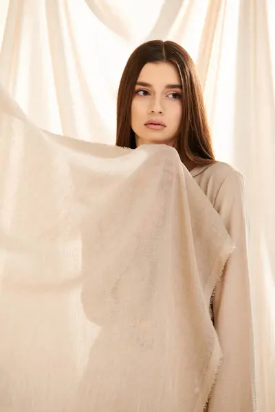 Una joven de pelo largo y morena posa en un atuendo veraniego, exudando elegancia y belleza frente a una cortina blanca. - foto de stock