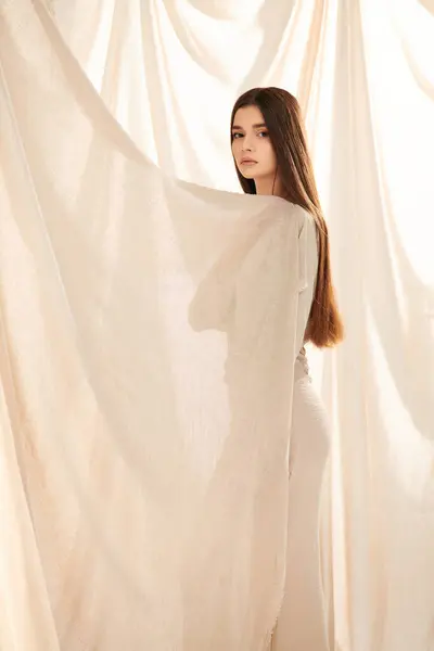 Молодая женщина с длинными брюнетками позирует перед белым занавесом, излучая летнее настроение в своем стильном наряде. — стоковое фото