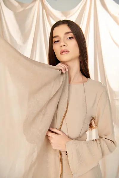 A young woman with long brunette hair strikes a pose in a summer outfit, exuding a summery mood against a white curtain. — Stock Photo