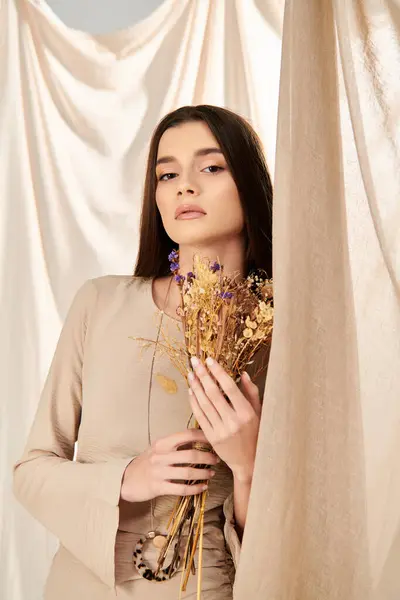 A young woman with long brunette hair holds a bunch of dried flowers, exuding a summery vibe in the studio. — Stock Photo