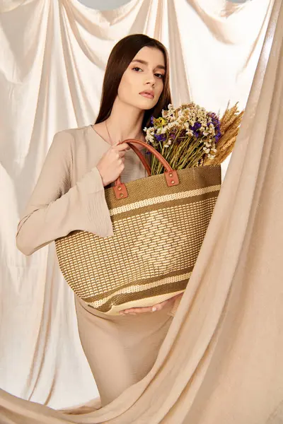 Una joven con el pelo largo morena posa en un traje de verano, delicadamente sosteniendo una cesta llena de flores de colores. - foto de stock