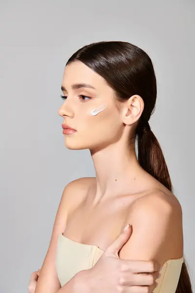 Una joven con el pelo morena aplicándose crema en la cara, exudando amor propio en un ambiente de estudio. - foto de stock