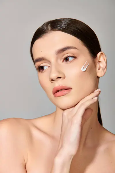A young woman with brunette hair posing in a studio, with white face cream delicately applied to her cheek. — Stock Photo