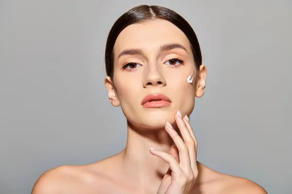 A brunette woman with clear skin delicately touches her face with face cream exuding confidence and elegance. — Stock Photo