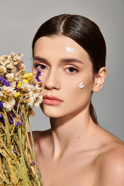 Молодая женщина с брюнетками держит яркий букет цветов, излучающих красоту и элегантность в студии на сером фоне. — стоковое фото