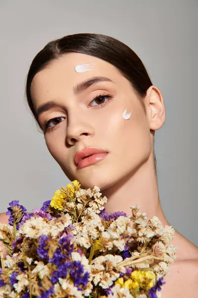 Eine brünette junge Frau strahlt Schönheit aus, während sie zärtlich einen Strauß lebendiger Blumen in einem Studio vor grauem Hintergrund hält. — Stockfoto