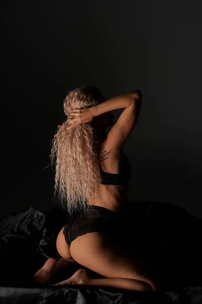 Una donna seducente in lingerie si siede provocatoriamente su un letto, trasudando un'aura di sensualità e fascino. — Foto stock