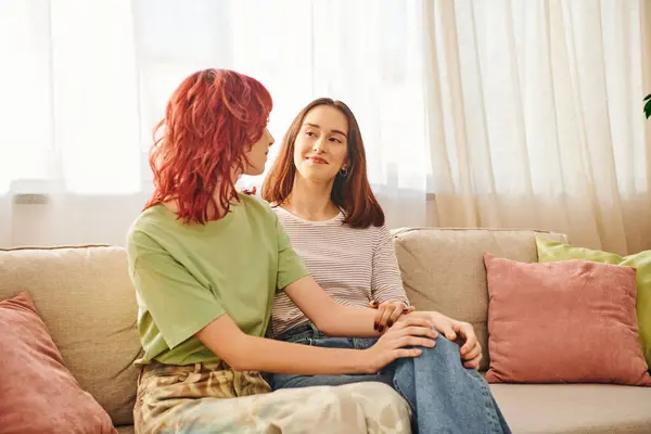 Dos jóvenes lesbianas compartiendo un tierno momento en un acogedor sofá, pareja encerrada en una mirada amorosa - foto de stock