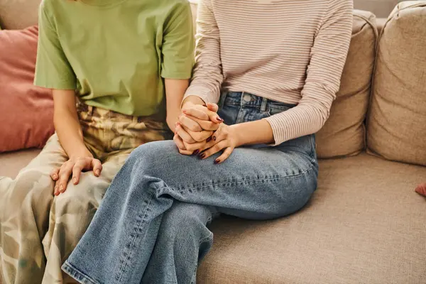 Close-up view of cropped lesbian couple holding hands and sitting on sofa, love and comfort at home — Stock Photo