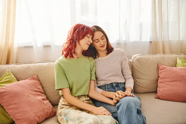 Tenderness, young and pleased lgbt couple in casual attire holding hands and sitting on sofa — Stock Photo