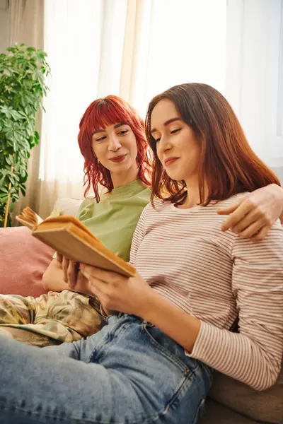 Alegre pareja de lesbianas disfrutando de un momento tranquilo de lectura juntos, envueltos en amor y comodidad - foto de stock