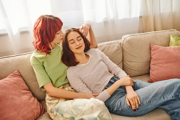 Happy lesbian couple in her 20s enjoying time together while resting on sofa in living room, bliss — Stock Photo