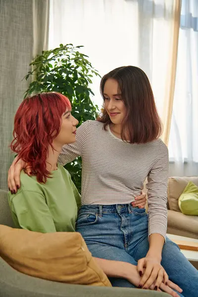 Glückliche lesbische Frau in ihren Zwanzigern, die auf dem Schoß ihrer Freundin sitzt, während sie Zeit im Wohnzimmer verbringt — Stockfoto
