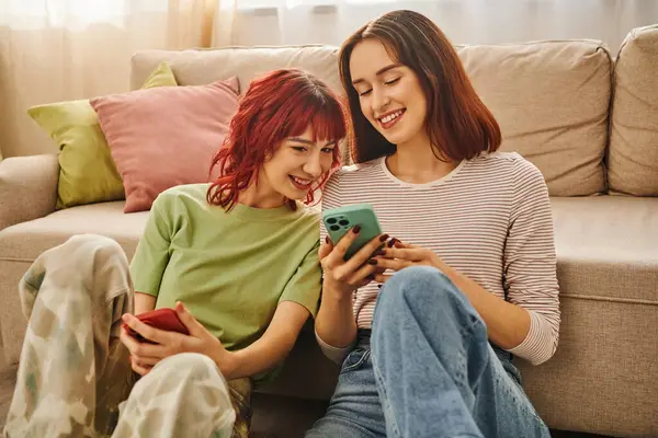 Щаслива лесбіянка пара посміхається і використовує смартфони у вітальні, сучасному способі життя та соціальних медіа — стокове фото