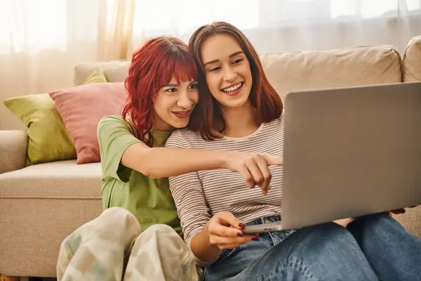 Heureux moment de joyeux couple lesbien pointant vers ordinateur portable et regarder le film dans le salon — Photo de stock
