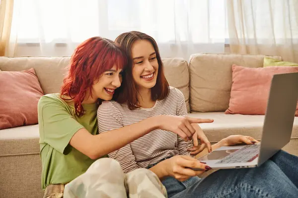 Heureux moment de sourire couple lesbien pointant vers ordinateur portable et regarder le film dans le salon — Photo de stock