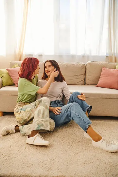 Happy young woman touching face of her beautiful girlfriend while sitting on carpet in living room — Stock Photo