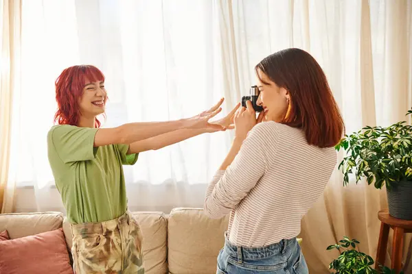 Home photo session of young lesbian woman capturing her girlfriend pose with outstretched hands — Photo de stock