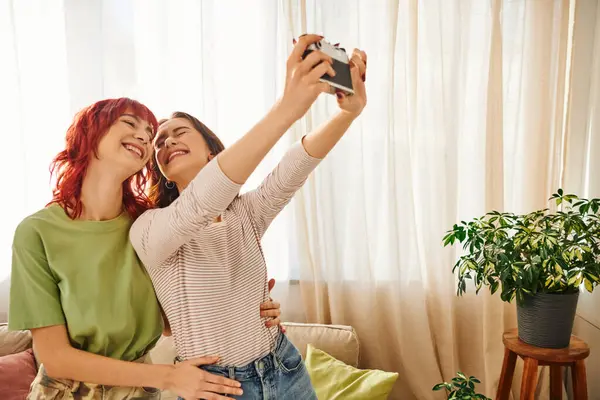 Home photo session of happy lesbian couple taking selfie on retro camera, capturing blissful moment — Foto stock