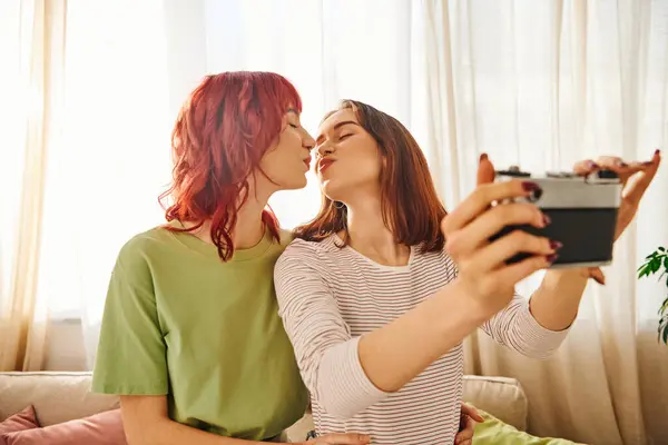 Junges lesbisches Paar küsst und macht Selfie mit Retro-Kamera und fängt glückselige Momente zu Hause ein — Stockfoto