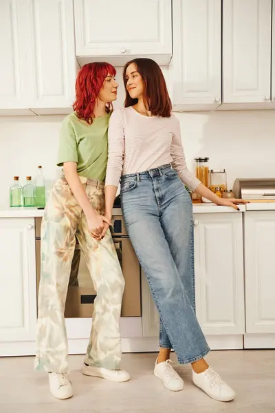 Escena de cocina íntima con una joven pareja lesbiana cariñosa compartiendo un momento de conexión, tomados de la mano - foto de stock