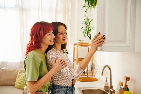 Affectionate young lesbian couple opening white kitchen cabinet and smiling together, domestic life — Stock Photo