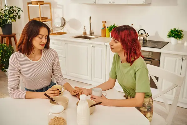 Kuscheliger Moment eines jungen lesbischen Paares, das sich beim Frühstück in einer gemütlichen Küche an den Händen hält — Stockfoto