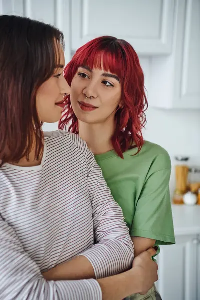 Retrato de mulher lésbica feliz e perfurada com cabelo vermelho olhando para sua namorada em casa — Fotografia de Stock