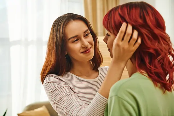 Happy young lesbian woman adjusting red hair of her cheerful girlfriend in modern apartment — Stock Photo