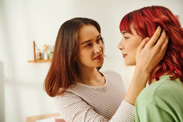 Jeune femme lesbienne ajuster les cheveux rouges de sa petite amie gaie dans un appartement moderne, bonheur — Photo de stock