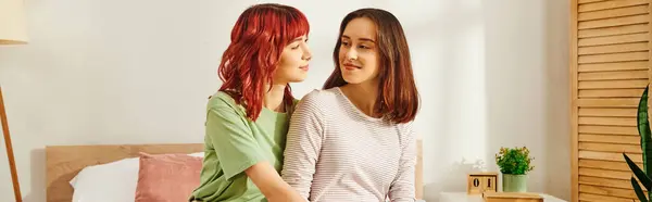 Young lesbian couple in casual attire sharing a cozy moment in sunny bedroom morning, banner - foto de stock