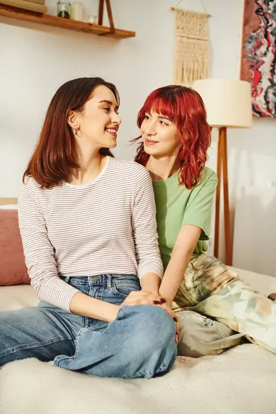 Young lgbt couple in casual attire sharing cozy moment and looking at each other in sunny bedroom — Stock Photo